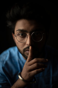 Fashion portrait of young and handsome Indian Bengali brunette man with traditional cotton wear and glasses holding pencil in black copy space background. Indian lifestyle and fashion photograph