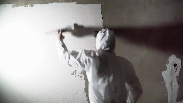 Construction worker plastering and smoothing concrete wall with putty. Putty and leveling walls for subsequent painting. Worker making repair in room. Builder using plastering tool for finishing wall