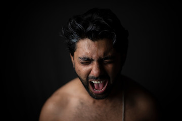 Portrait of young and handsome Indian Bengali brunette man in bare body crying loudly in black copy space background. Indian lifestyle and fashion photography