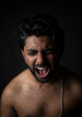 Portrait of young and handsome Indian Bengali brunette man in bare body crying loudly in black copy space background. Indian lifestyle and fashion photography