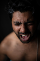 Portrait of young and handsome Indian Bengali brunette man in bare body crying loudly in black copy space background. Indian lifestyle and fashion photography