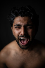 Portrait of young and handsome Indian Bengali brunette man in bare body crying loudly in black copy space background. Indian lifestyle and fashion photography