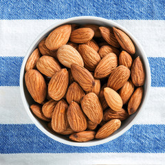 peeled almonds in a white bowl on a background of striped blue and white fabric, square cropping