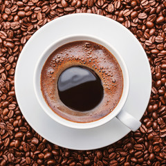 black coffee with froth in a white cup top view on a background of scattered coffee beans. square cropping