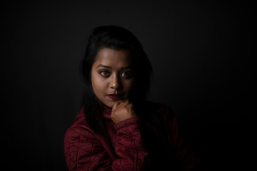 Fashion portrait of an young Indian Bengali brunette woman with maroon winter jacket in black copy space background. Indian lifestyle and fashion photography.