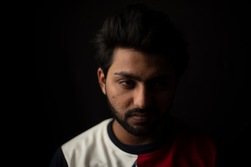 Fashion portrait of young and handsome Indian Bengali brunette man with casual tee shirt showing facial expression in black copy space background. Indian lifestyle and fashion photography