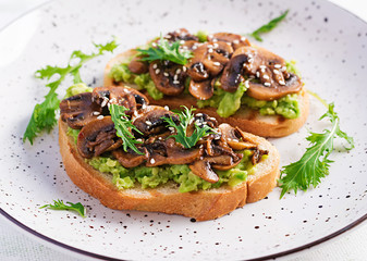 Bruschetta. Sandwich with avocado, fried mushrooms, sesame on a white table. Vegetarian food. Vegan menu.