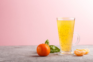 Glass of tangerine orange colored drink with basil seeds on a gray and pink background. Side view