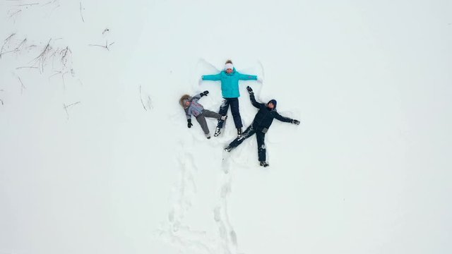 A family with children makes a figure of a snow angel in a clearing in the forest. Aerial photography of a girl and children lying in the snow.