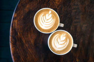Two cups of cappuccino with latte art on brown wooden background. Perfect foam, top view, place for text.