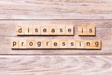 disease is progressing word written on wood block. disease is progressing text on wooden table for...