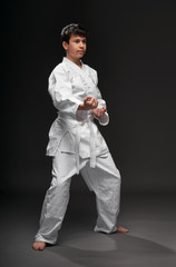 a teenager dressed in martial arts clothing poses on a dark gray background, a sports concept