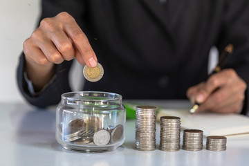 The coin in a glass jar is about to drop a coin with a record of income and expenses. The idea of saving money to buy a house for the future. Mortgage home and real estate.