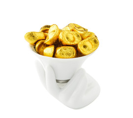 Ancient Chinese gold money (gold ingot ornaments) made from chocolate put in a white cup which holding by hand isolated on white background .