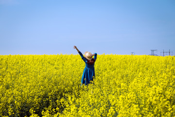 Naklejka na ściany i meble girl walking in a field of yellow rapeseed