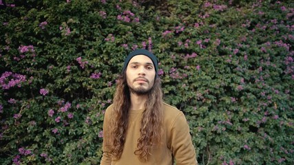 Portrait of long haired hipster walking near parkt in modern city in slow motion. Stylish man near nature