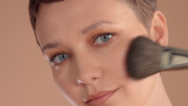 Closeup caucasian woman put sma makeup powder to her cheek bone with a brush