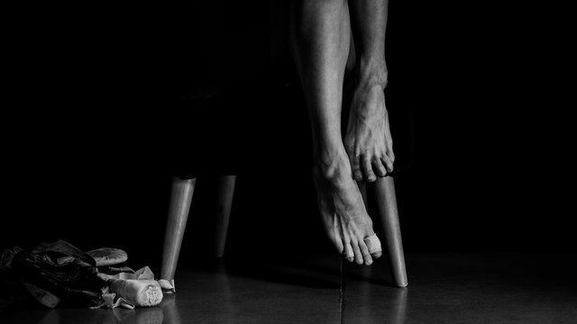 Close-up ballerina's bare foot when she is sitting next to her old dance slippers, high contrast black and white studio shot