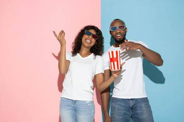 Watching cinema, crazy happy. Young man and woman in casual clothes on pink, blue bicolored background. Concept of human emotions, facial expession, relations, ad. Beautiful african-american couple.