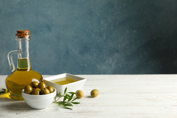 Jug with olive oil and bowl with olives on wooden table, space for text