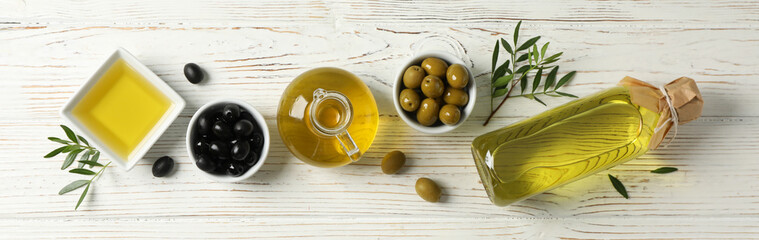 Flat lay with bottle, jug, bowl with olive oil and olives on wooden background, space for text
