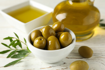 Bottle and bowl with olive oil, bowl with olives on wooden background, close up