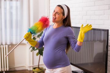 Beautiful pregnant woman enjoys cleaning her house.