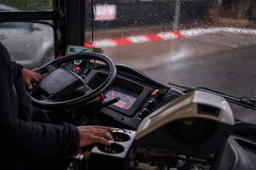 The drivers cab of the public bus, his hand on the drivers wheel, outside the window - it s rainy. Close-up.