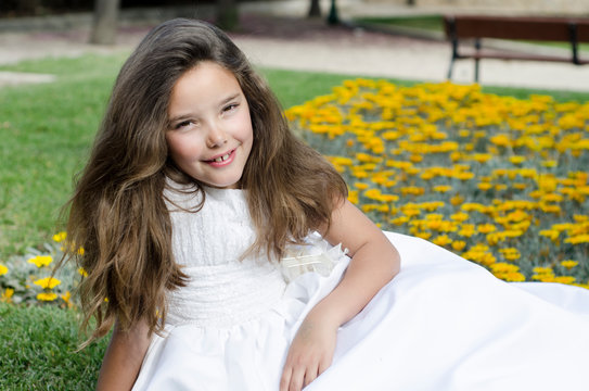 Portrait of little girl lying down with her white dress near the flowers. Ready to take her first communion
