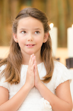 Little girl pray putting her hands together in celebration of her first communion inside the church