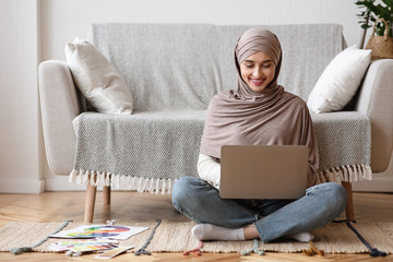 Millennial Muslim Girl Sitting On Floor With Laptop On Lap