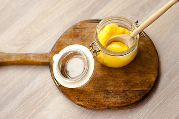 Ghee clarified butter desi in glass jar with spoon made from wood on natural wooden background