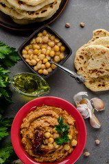 Hummus topped with chickpeas, sun dried tomatoes and green coriander leaves on stone table with pita bread aside