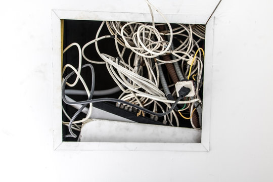 Electrical installation, wires stick out of the hole in the ceiling construction. A tangle of communication wires hang from a hole in the ceiling.