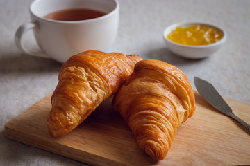 Fresh croissants on wooden board with orange jam in bowl and tea cup