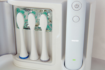 An electric toothbrush with replaceable attachments of tooth brush stored in a UV disinfection stand, on the handle lights the WHITEN option. The kit for tooth cleaning with vibration and sonic.