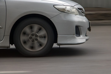 Detail of front of car driving on asphalt. Car front wheel rotates on road, motion blurred background.