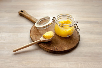 Ghee clarified butter desi in glass jar with spoon made from wood on natural wooden background
