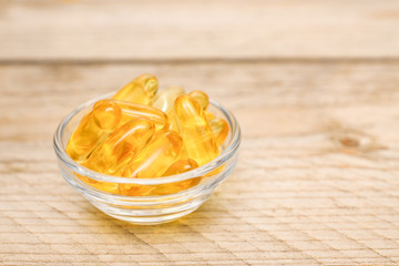 glass bowl with fish oil capsules on wooden background