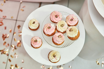 Pink and beige vanilla cupcakes on glass stand, copy space. Dessert table for party. Holiday concept