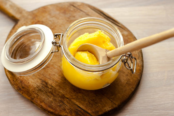 Ghee clarified butter desi in glass jar with spoon made from wood on natural wooden background