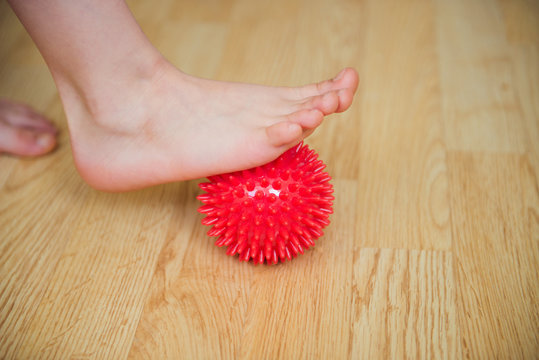 kid's foot with red massage ball- orthopedic correction of flat feet