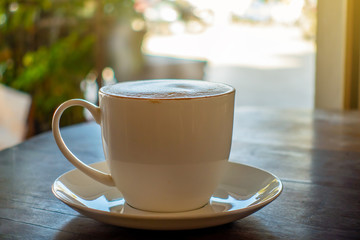 The white ceramic of hot cappuchino or latte on the table with the natural warm light flare in the morning.