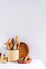 Fototapeta na wymiar Wooden set of kitchenware in iron cup with wooden plates on white textile table. Cooking appliances. Zero waste