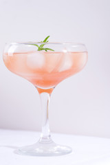 Pink cocktail with rosemary and ice on a white tablecloth on the table