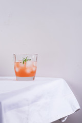 Pink cocktail with rosemary and ice in glass on a white tablecloth on the table