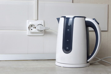 White electric kettle stands on a gray table plugged into a power outlet