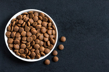 Dry pet food in a white ceramic bowl on black background