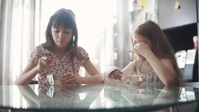 child with a broken arm in a bandage draws with pencils. two little girls schoolgirls draw together sitting at the table at home.