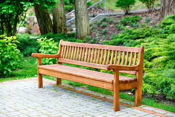 Fototapeta na wymiar A beautiful and elegant oak bench stands in a park in a recreation area on paving slabs.